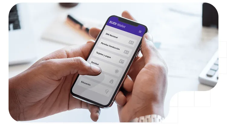 Primer plano de unas manos sosteniendo un teléfono móvil que muestra la pantalla principal de la aplicación EUDI Wallet.
